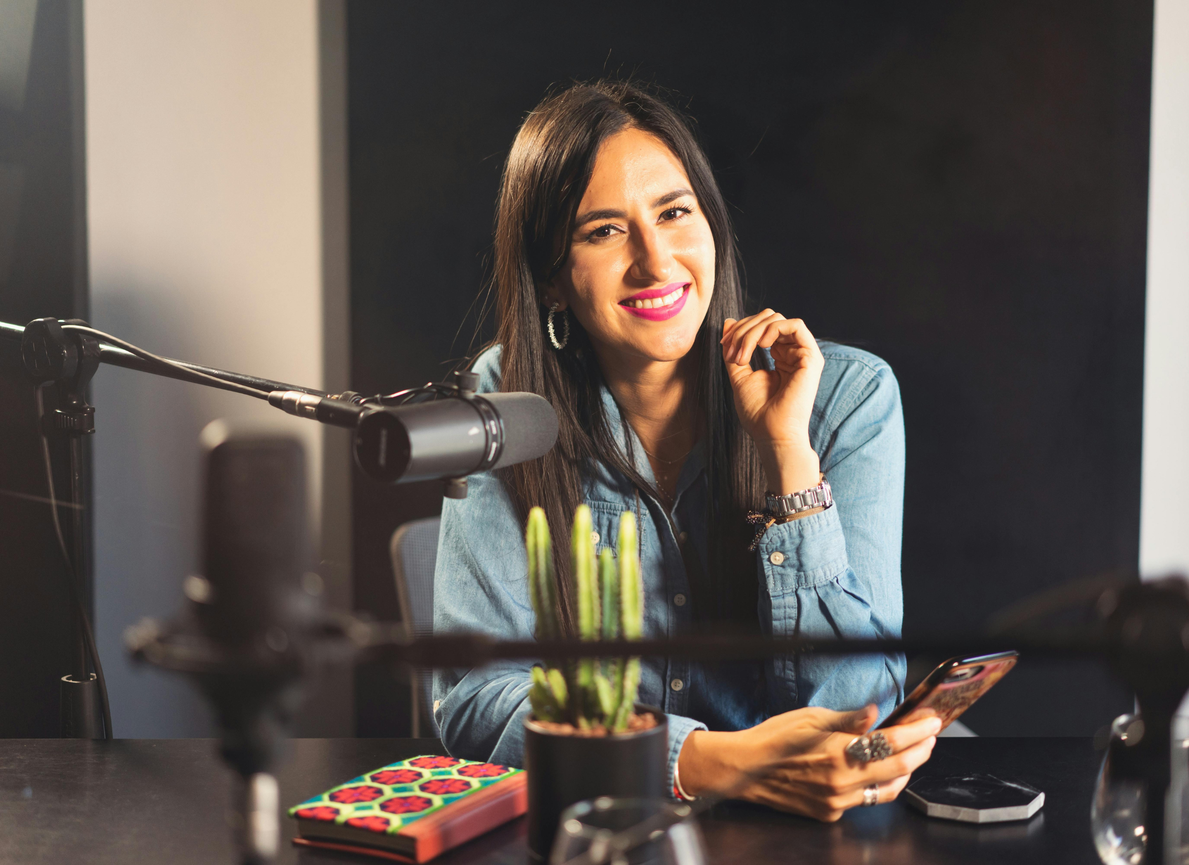 A Smiling Woman Sitting Near the Microphone while Holding Her Phone